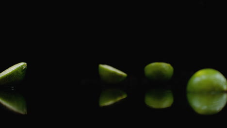 Several-green-ripe-limes-fall-on-the-glass-with-splashes-of-water-in-slow-motion-on-a-dark-background
